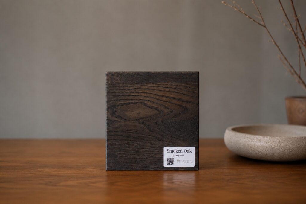 Ciemna próbka drewna Smoked Oak marki Patrei na drewnianym stole w minimalistycznej aranżacji